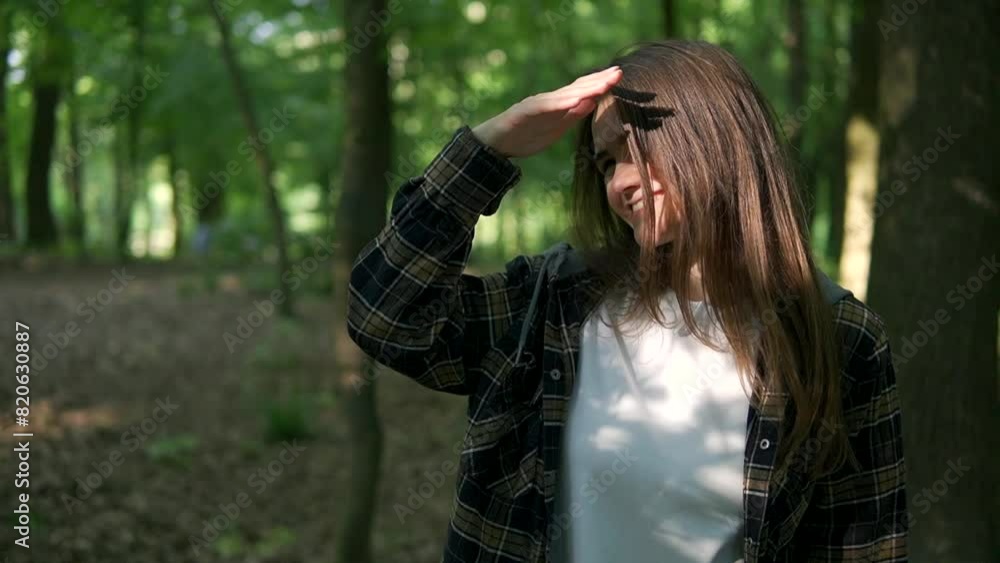 A young smiling girl with a beautiful smile was blinded by the sun in a green forest. She is wearing a white T-shirt and a plaid shirt. Athletic build. A young smiling girl with a beautiful smile was blinded by the sun in a green forest. She is wearing a white T-shirt and a plaid shirt. Athletic build.