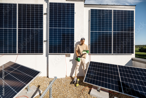 Technician with a digital tablet checks the operation of a newly installed solar station on the roof of a house. The concept of maintenance of solar plants and their performance photo