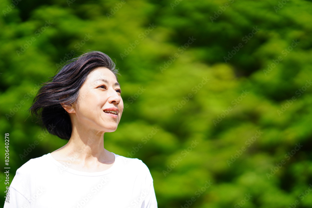 緑の中気持ちよさそうに髪を風になびかせる中年女性 緑の中気持ちよさそうに髪を風になびかせる中年女性
