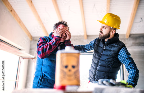 Colleague giving first aid to worker with chemical splashed on his skin, face. Accident at construction site Concept of occupational safety and health in workplace.