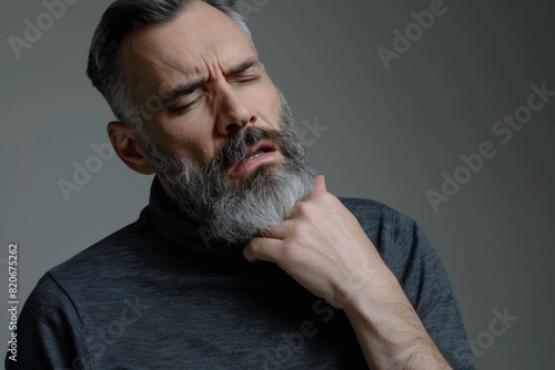Middle aged sick man having sore throat, looking at copy space over grey studio background. Bearded man touching his red neck, suffering from throat disorder, tonsillitis, throat cancer, cold photo