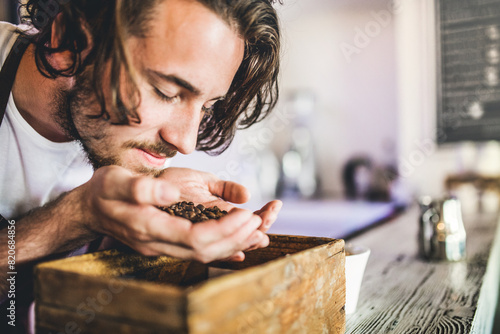 Obraz na plátně Handsome barista working in coffee shop, smelling coffee beans