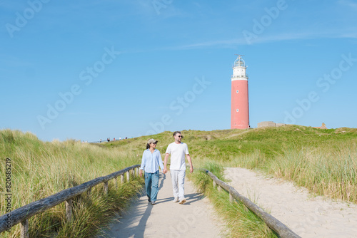 A couple leisurely walks along a path next to a charming lighthouse on the picturesque island of Texel, Netherlands. man and woman at The iconic red lighthouse of Texel Netherlands