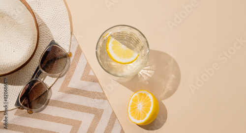 Summer layout with lemonade, fresh citrus fruits, hat and sunglasses on a beach towel on a beige background.