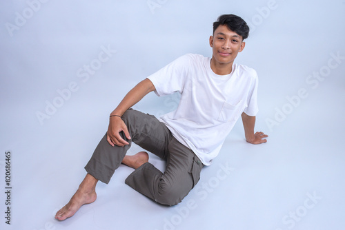Young Asian man wear white t-shirt sitting on the floor against grey background
