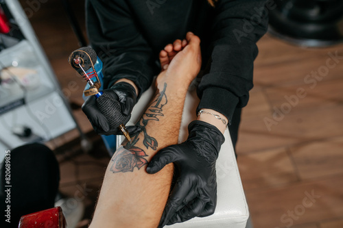 Close up tattoo master  professional tattoo artist in black gloves making a  rose tattoo on a man's forearm. © Med Photo Studio
