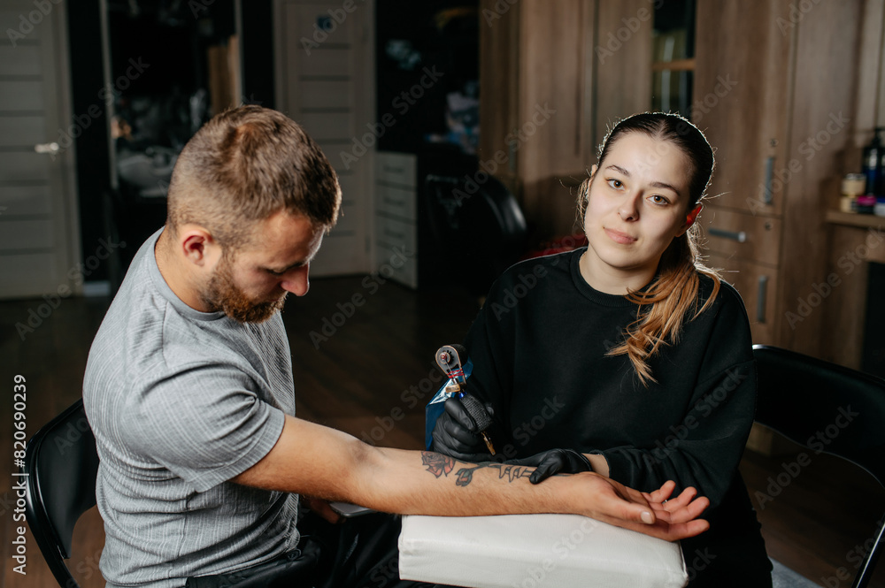Young woman professional tattoo artist in black gloves making a rose tattoo on a man's forearm. Young woman professional tattoo artist in black gloves making a rose tattoo on a man's forearm.