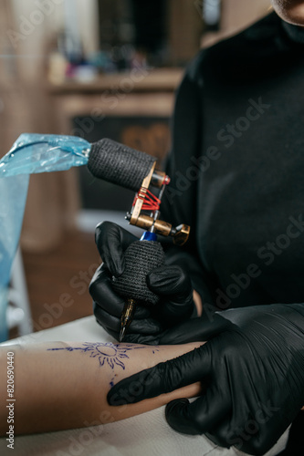 Close up young woman professional tattoo artist in black gloves making a  tattoo on a woman's  forearm