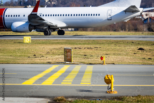 Runway holding point with stop bars and red lights. Airport safety installation. Jet departing on the runway in the background.