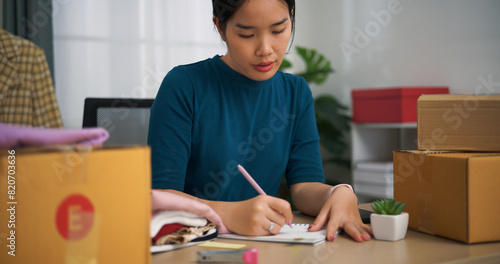 Portrait of Young asian woman business owner sitting at desk check and write orders customers into book ,Online Shopping