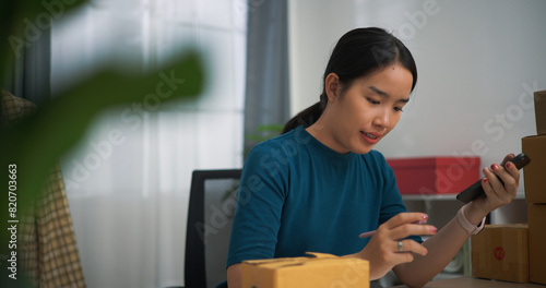 Portrait of Young asian woman business owner sitting at desk check orders by phone and write into book , Online Shopping