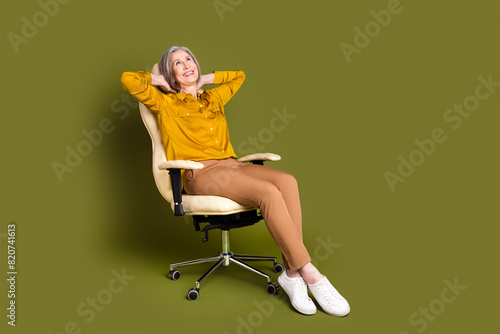 Full length photo of adorable positive woman wear shirt arms behind head looking empty space isolated khaki color background