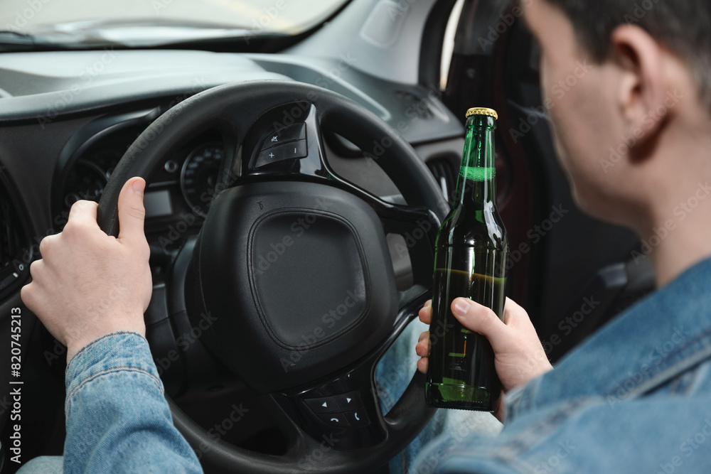 Man with bottle of beer driving car, closeup. Don't drink and drive concept Man with bottle of beer driving car, closeup. Don't drink and drive concept