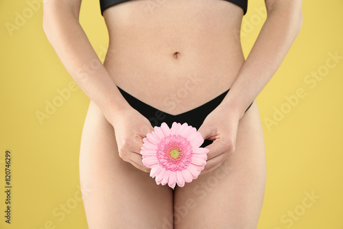 Gynecology. Woman in underwear with gerbera flower on yellow background, closeup