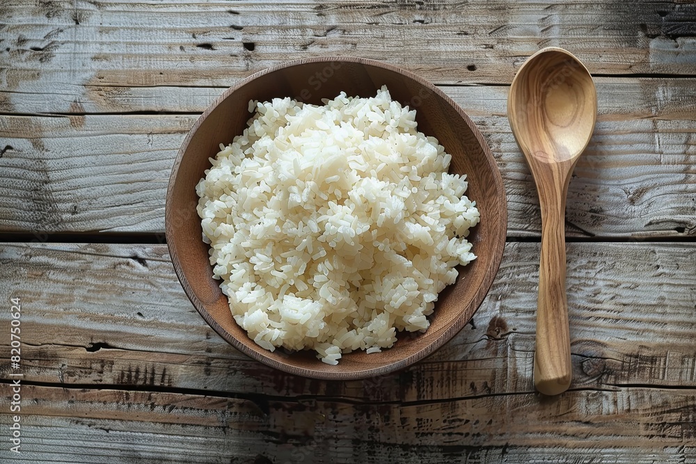 A wooden bowl filled with cooked white rice sits next to a wooden spoon on a wooden table. Generative AI A wooden bowl filled with cooked white rice sits next to a wooden spoon on a wooden table. Generative AI