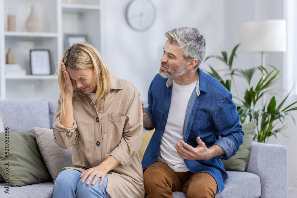A middle-aged couple is seen arguing in their living room, depicting emotions of frustration and sadness in a domestic environment. A middle-aged couple is seen arguing in their living room, depicting emotions of frustration and sadness in a domestic environment.