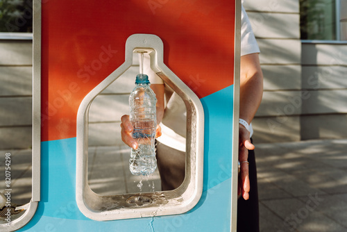 A woman pours drinking water into a water bottle in the city at a gas station. Sustainable consumption of resources and reduction of waste photo