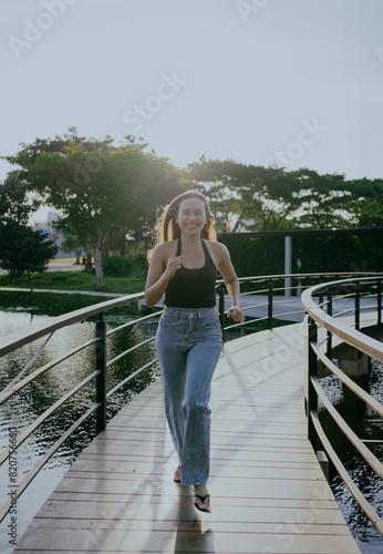 Happy Asian woman playing and running on city park bridge. Attractive Asian girl enjoying fun outdoor lifestyle on summer vacation.