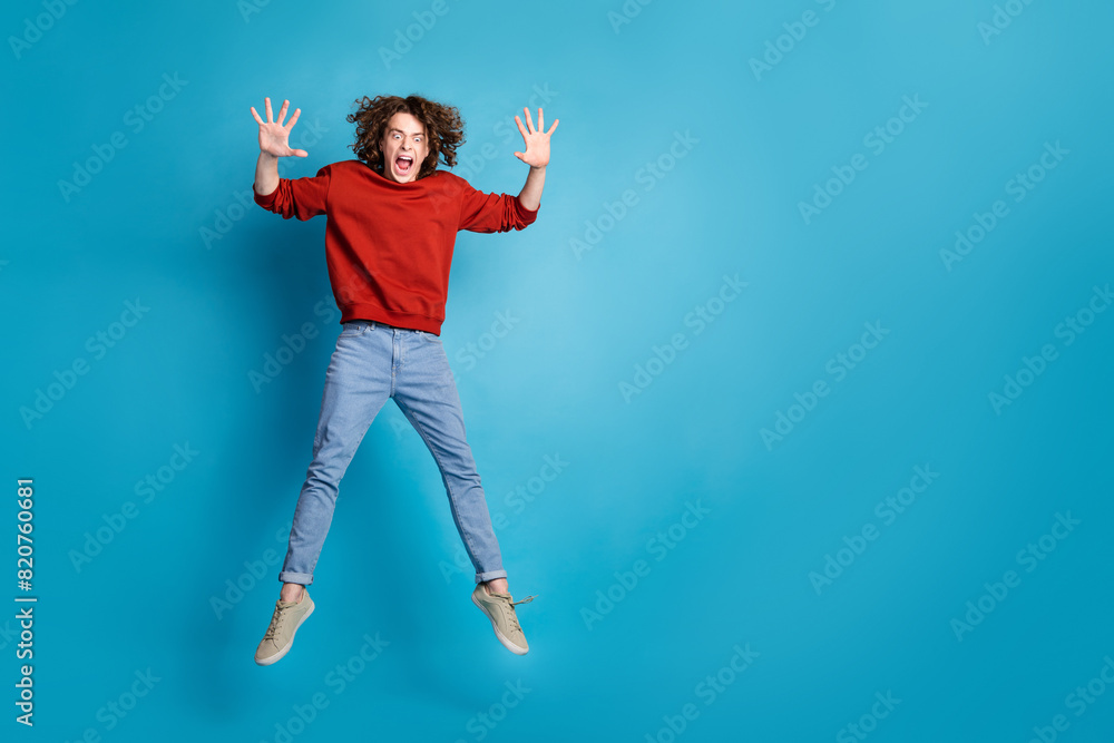 Full length photo of handsome scaring guy wear red sweater jumping high falling emtpy space isolated blue color background Full length photo of handsome scaring guy wear red sweater jumping high falling emtpy space isolated blue color background