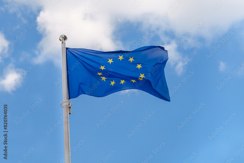 Close-up the flag of the EU, European Union flies against the background of a cloudy blue sky