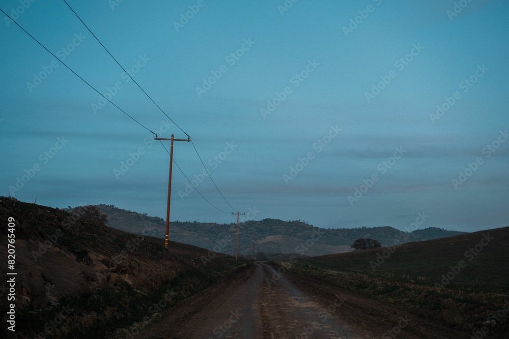 Rural dirt road with fading sunlight and power lines stretching across the scene. Rural dirt road with fading sunlight and power lines stretching across the scene.