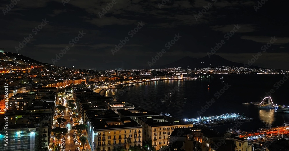 Fototapeta premium Aerial view of a cityscape near the shore, glowing with vibrant lights in the night