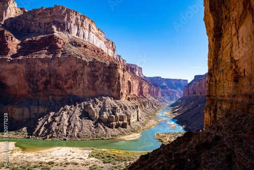 Mountain range on a sunny day, featuring rocky cliffs, lush greenery and a winding river