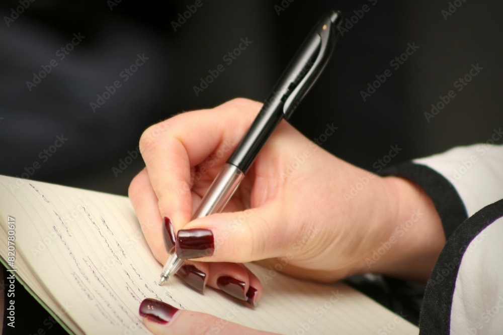 Close-up of a person's hands writing notes in a notebook, with a pen in her hand Close-up of a person's hands writing notes in a notebook, with a pen in her hand