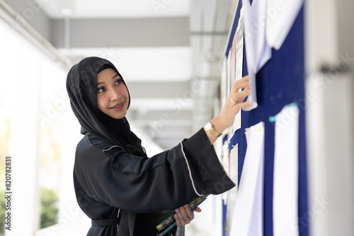 Принти на полотні Muslim student in university smiling wearing black niqab finding job looking at the billboard
