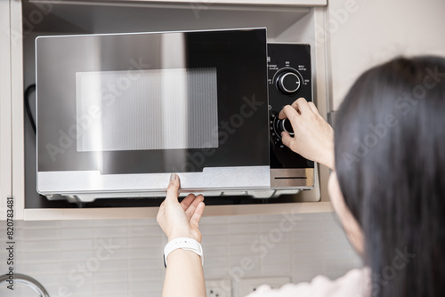 people using the microwave oven, women adjust time to reheat warm food in microwave.