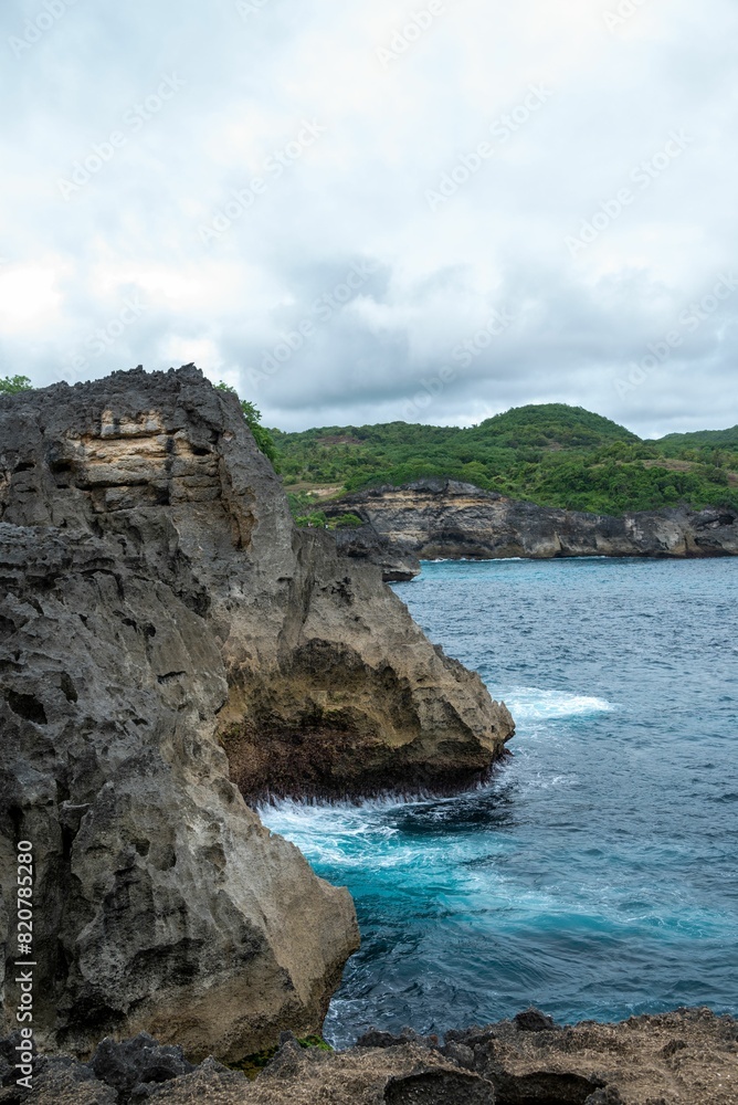 Blue ocean and cliffs with lush greenery against the background of a cloudy sky. Penida, Indonesia.