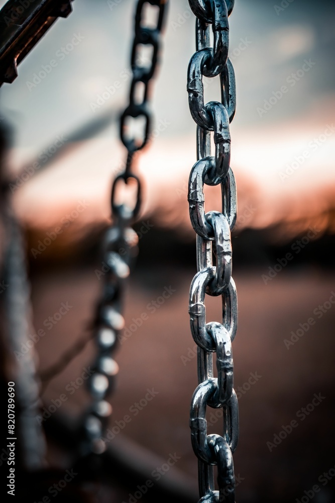 Closeup of a set of metal chains against a vibrant sunset in the background Closeup of a set of metal chains against a vibrant sunset in the background
