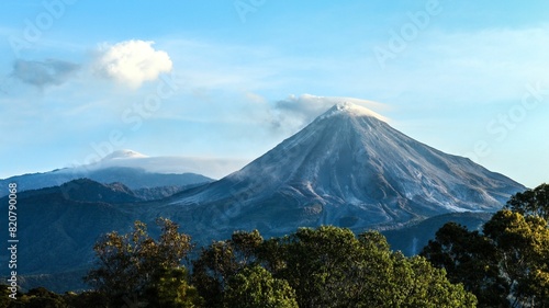 Colima's volcanoes at sunset exhaling a plume of smoke. © Wirestock