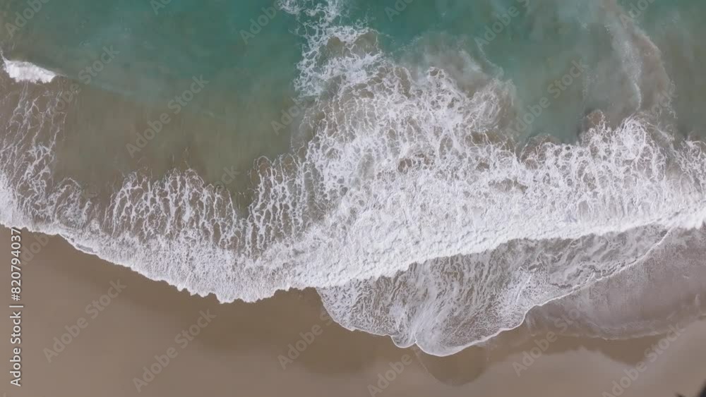 Plano cenital grabado con Drone de unas preciosas olas de agua azul llegando a la orilla cubriendo la dorada arena de la playa de Getaria en Gipuzkoa (País Vasco).