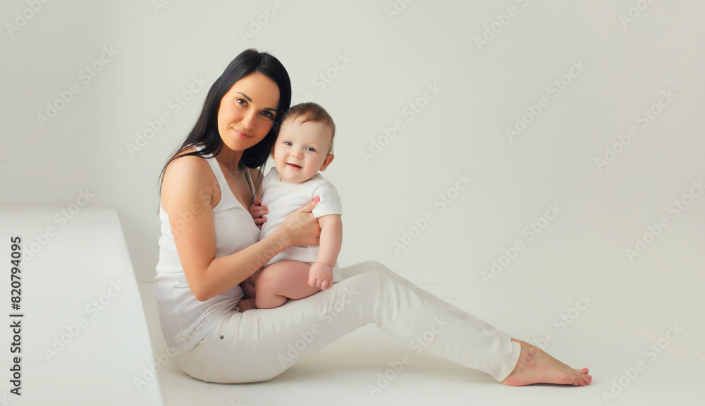 Happy young mother holding cute baby together in white room at home Happy young mother holding cute baby together in white room at home