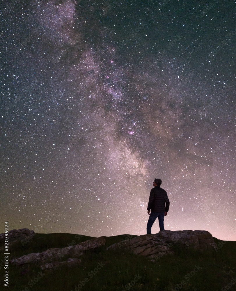 Fototapeta premium Mature man stands on a hilltop, with a magical star-filled night sky visible in the background