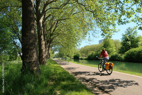 Cyclotourisme dans la campagne, sur une piste cyclable bordée d’arbres, au bord du canal de Bourgogne à Dijon, en Côte d’Or, paysage de nature avec une femme cycliste sur un vélo de randonnée (France)