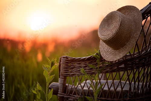 straw hat on an old wicker chair in a field overlooking the sunset on a summer evening.