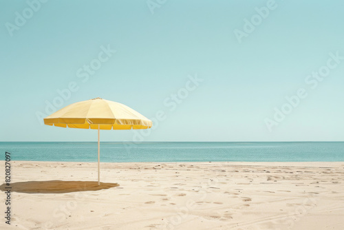 A lone yellow beach umbrella stands on an empty  sandy shore against a serene ocean backdrop