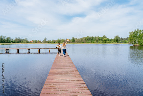 Rear view of two girls running playing on wooden dock by calm lake, enjoying serene atmosphere under clear blue sky
