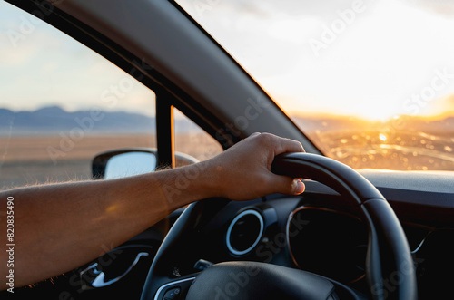 A man's hand on the steering wheel. Driving during sunset