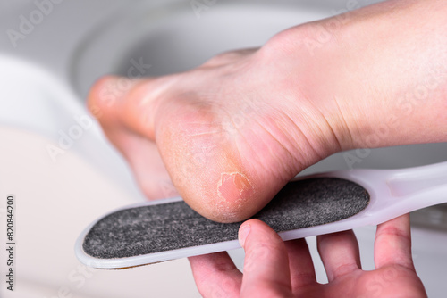 Woman's hands cleaning the heel with pumice in the bathroom.