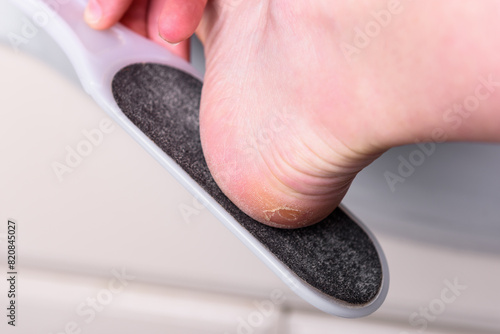 Woman's hands cleaning the heel with pumice in the bathroom.