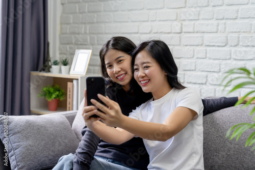 Asian lesbian couple Two happy Asian girls smiling at home sit and take pictures together at home. LGBT lesbian moments.
