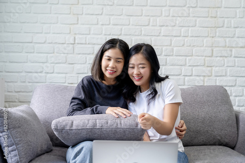 Smiling Asian lesbian couple using tablet for entertainment on sofa at home. LGBT lesbian moments.