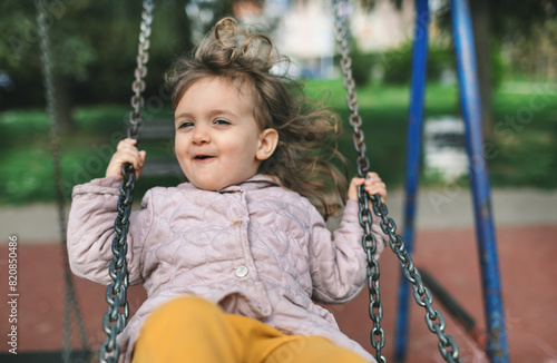 Littler girl swing and laughing at playground. Happy toddler kid playing.