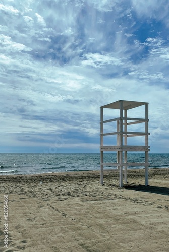 Empty lifeguard tower on a deserted sandy beach with calm sea and cloudy sky. Peaceful seascape with no people