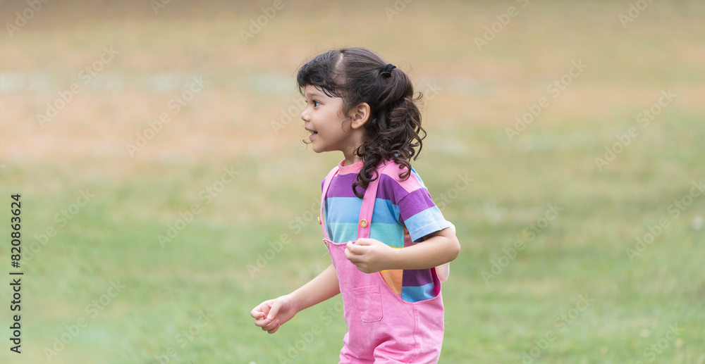 Portrait of Caucasian child girl in park playing outdoor in nature. Little girl standing, laughing, smiling in casual clothes. Education, healthy activities. Side view Portrait of Caucasian child girl in park playing outdoor in nature. Little girl standing, laughing, smiling in casual clothes. Education, healthy activities. Side view
