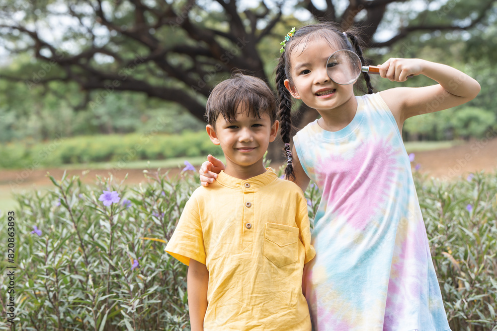 Portrait of Asian and Caucasian children friends in park playing together outdoor in nature. Little boy and girl standing, holding and looking through magnifying glass, smiling in casual clothes Portrait of Asian and Caucasian children friends in park playing together outdoor in nature. Little boy and girl standing, holding and looking through magnifying glass, smiling in casual clothes