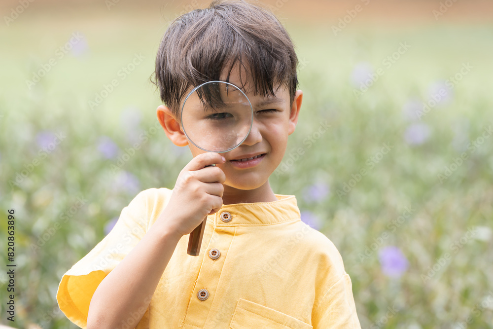 Portrait of Caucasian child boy in park playing outdoor in nature. Little boy standing, holding and looking through magnifying glass, curious smiling in casual clothes. Education Portrait of Caucasian child boy in park playing outdoor in nature. Little boy standing, holding and looking through magnifying glass, curious smiling in casual clothes. Education